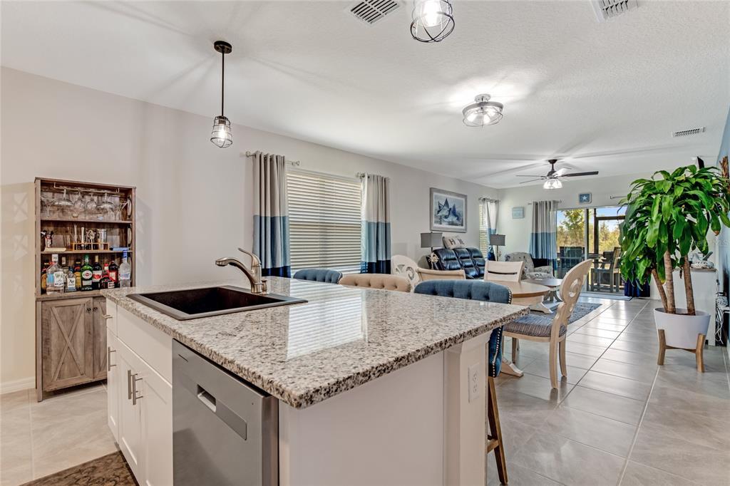 A kitchen island with a granite countertop and sink overlooks an open-concept living and dining area — 1362 CORK DRIVE, ORMOND BEACH, FL