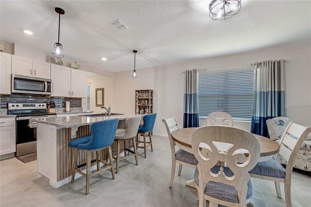 A kitchen with a granite island, bar stools, and an adjacent dining area with chairs — 1362 CORK DRIVE, ORMOND BEACH, FL