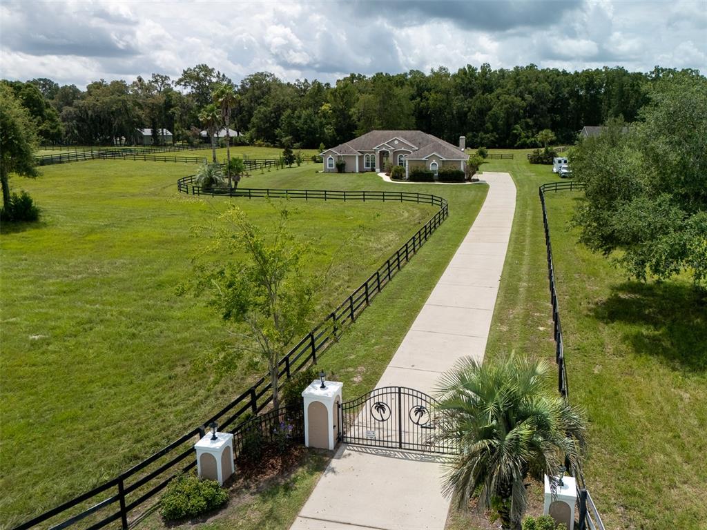 An aerial view shows a gated concrete driveway leading to a house surrounded by fenced pastures — 1500 NW 114TH LOOP, OCALA, FL