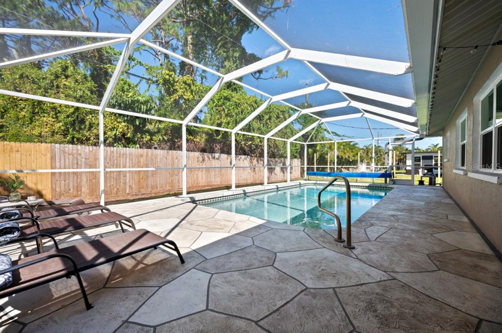A screened-in pool patio features stone-patterned concrete flooring and three lounge chairs — 874 ACADIA ROAD, VENICE, FL