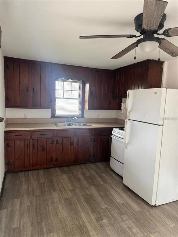 A kitchen features dark wood cabinets, a white refrigerator, a double sink, and wood-look flooring — 311 NE SANCHEZ AVENUE, OCALA, FL