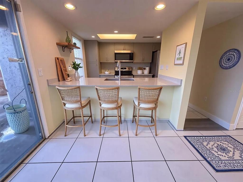 A kitchen features a breakfast bar with three wicker stools and light-colored cabinetry — 4033 HENLEY ROAD UNIT 1707, ORLANDO, FL