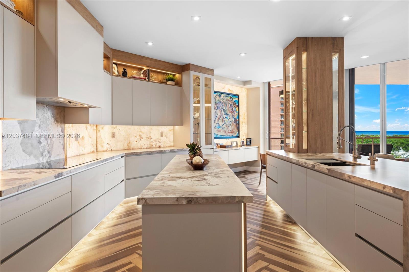 A modern kitchen features light cabinetry, marble countertops, under-cabinet lighting, and a view of the ocean — 60 Edgewater Dr # 11F, Coral Gables FL 33133, CORAL GABLES, FL