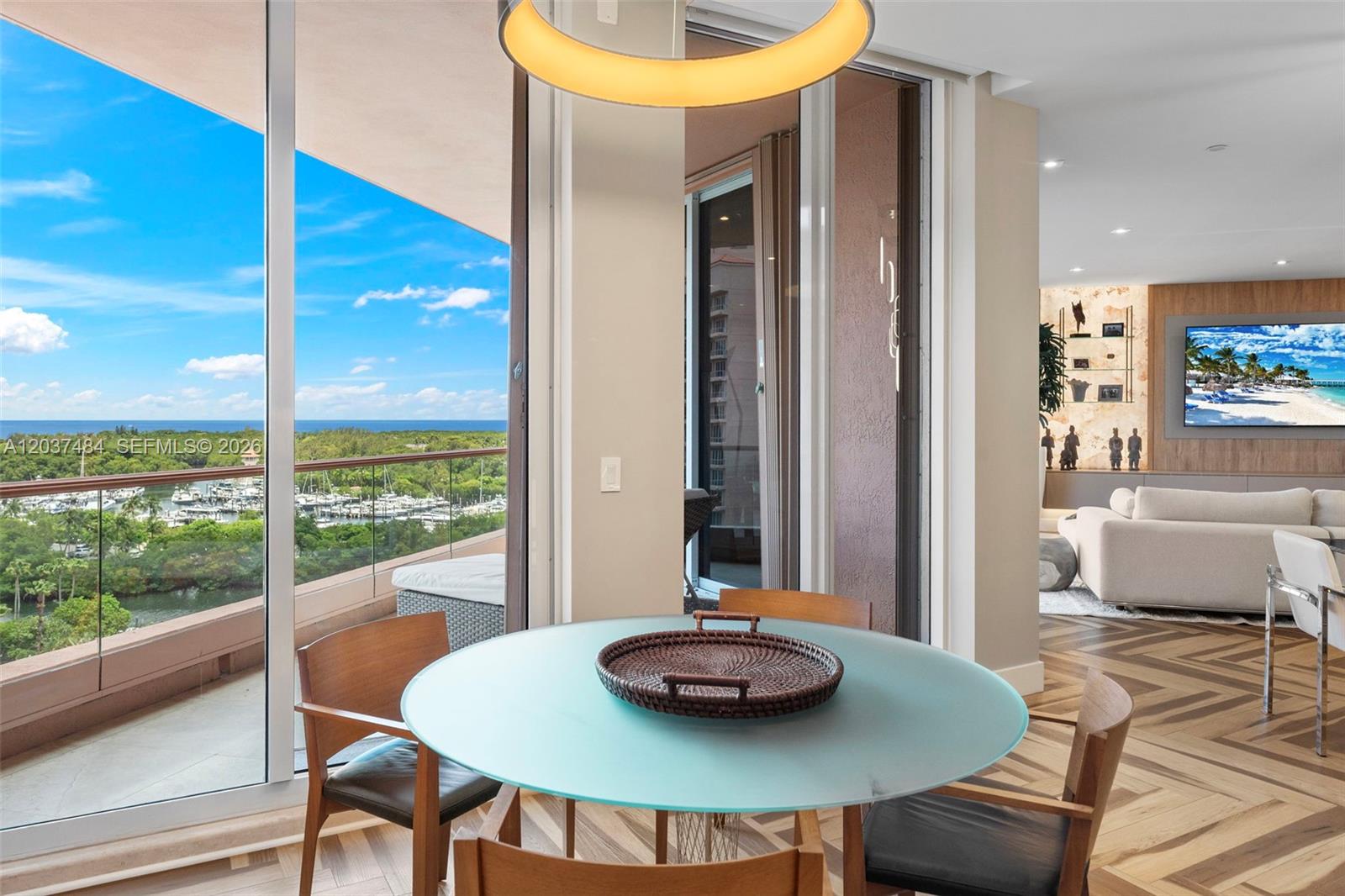 A dining area with a glass table overlooks a balcony, marina, and the ocean — 60 Edgewater Dr # 11F, Coral Gables FL 33133, CORAL GABLES, FL