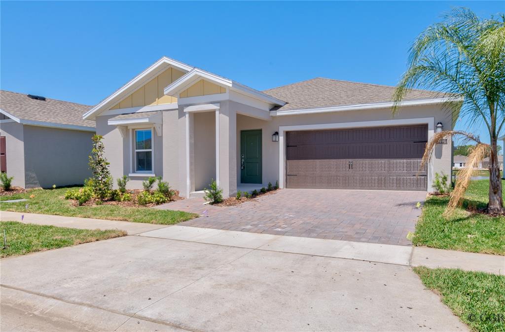 A single-story house with a beige stucco exterior, a green front door, and a paved driveway — 1496 BRENTWOOD DRIVE, KISSIMMEE, FL