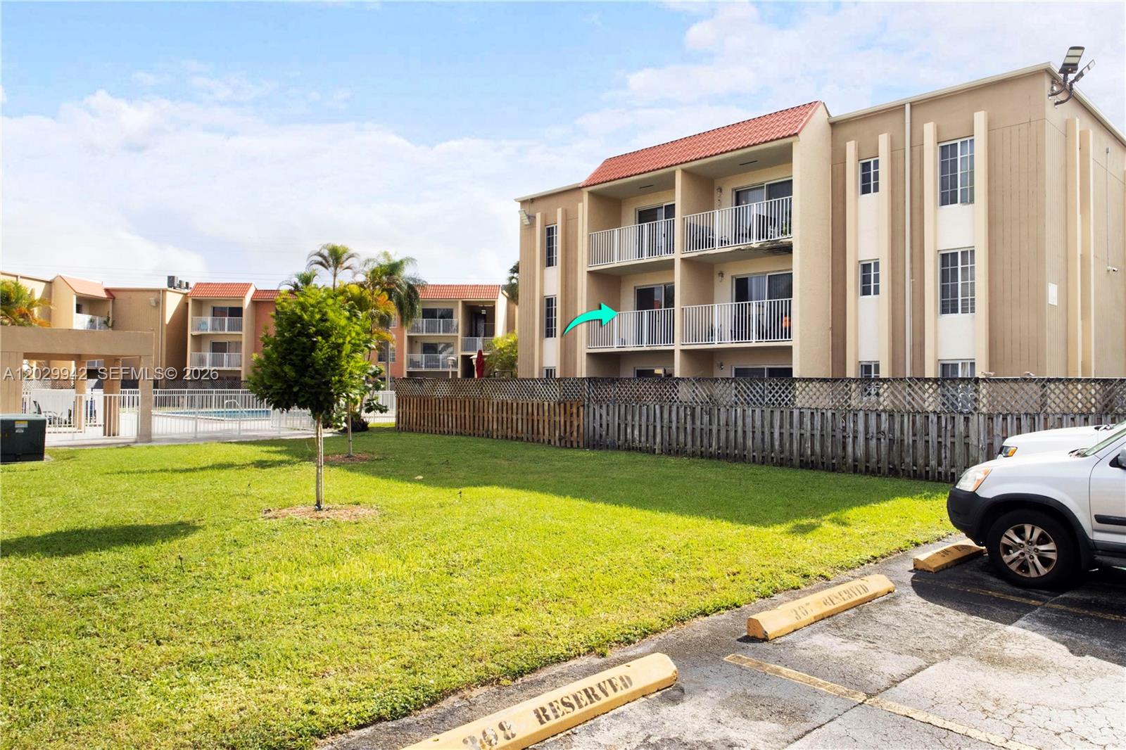 A multi-story apartment building features balconies and a parking lot in the foreground — DORAL, FL