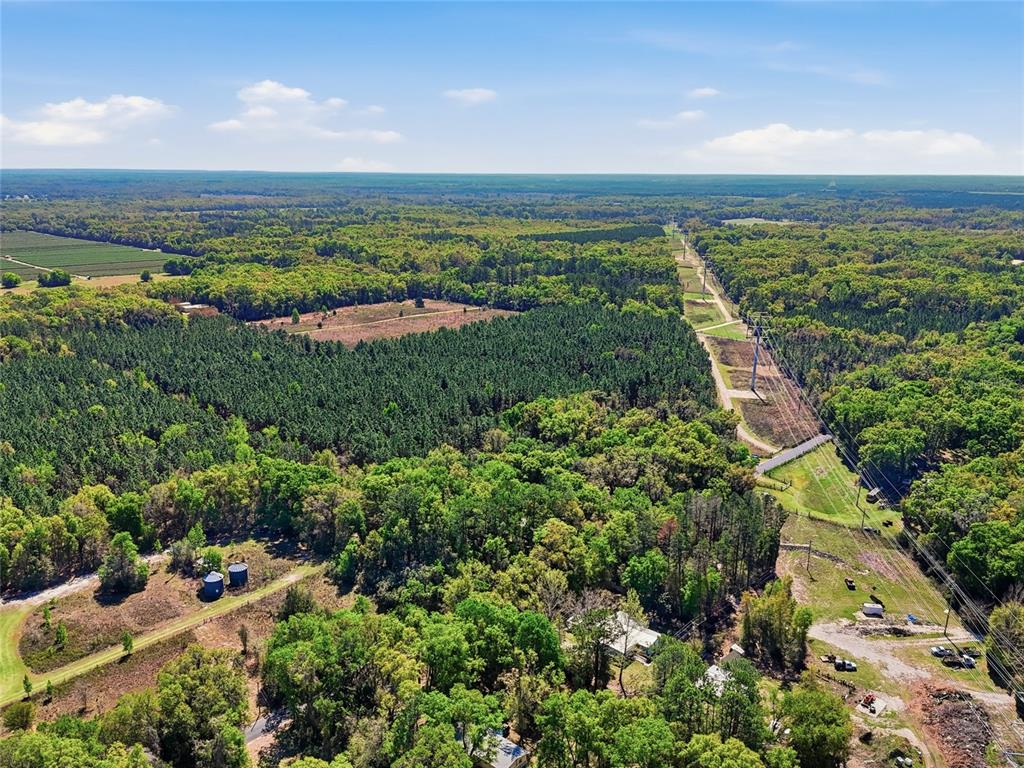An aerial view shows a rural landscape with dense forests, a power line corridor, and buildings — 11791 SW 143RD STREET SW, ARCHER, FL