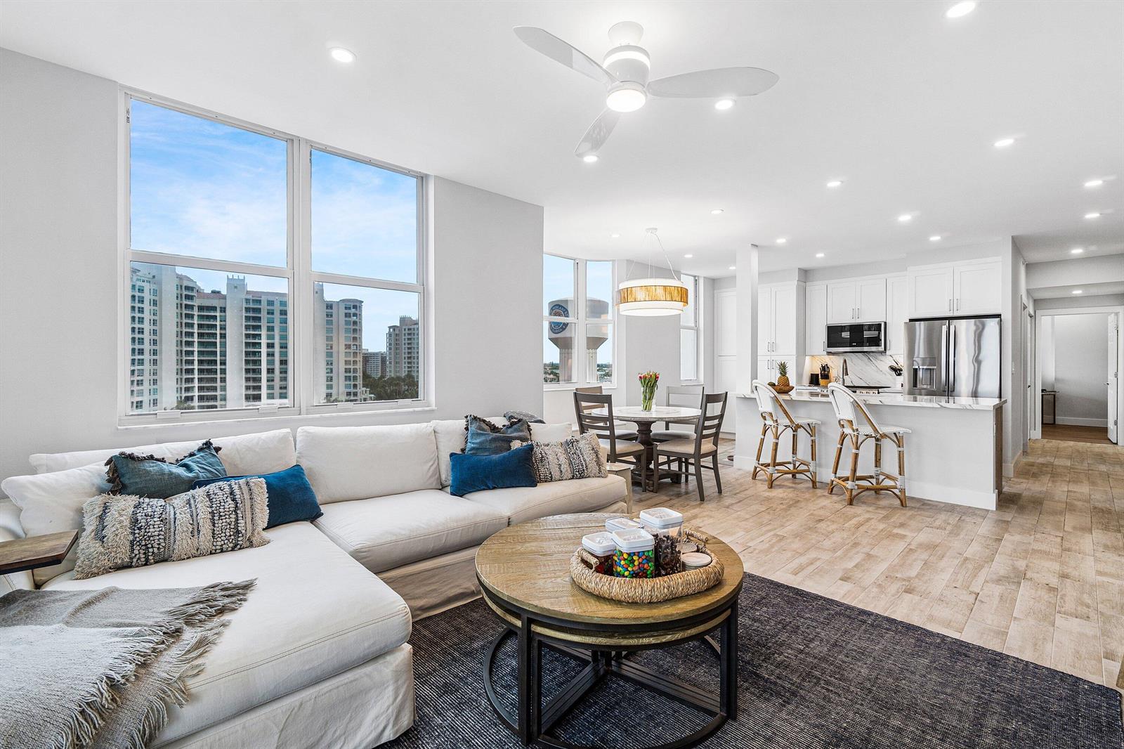 A bright, open-concept living and dining area features a white sectional, wood-topped coffee table, and kitchen — 3606 S Ocean 1002 Boulevard # 1002, Highland Beach FL 33487, HIGHLAND BEACH, FL