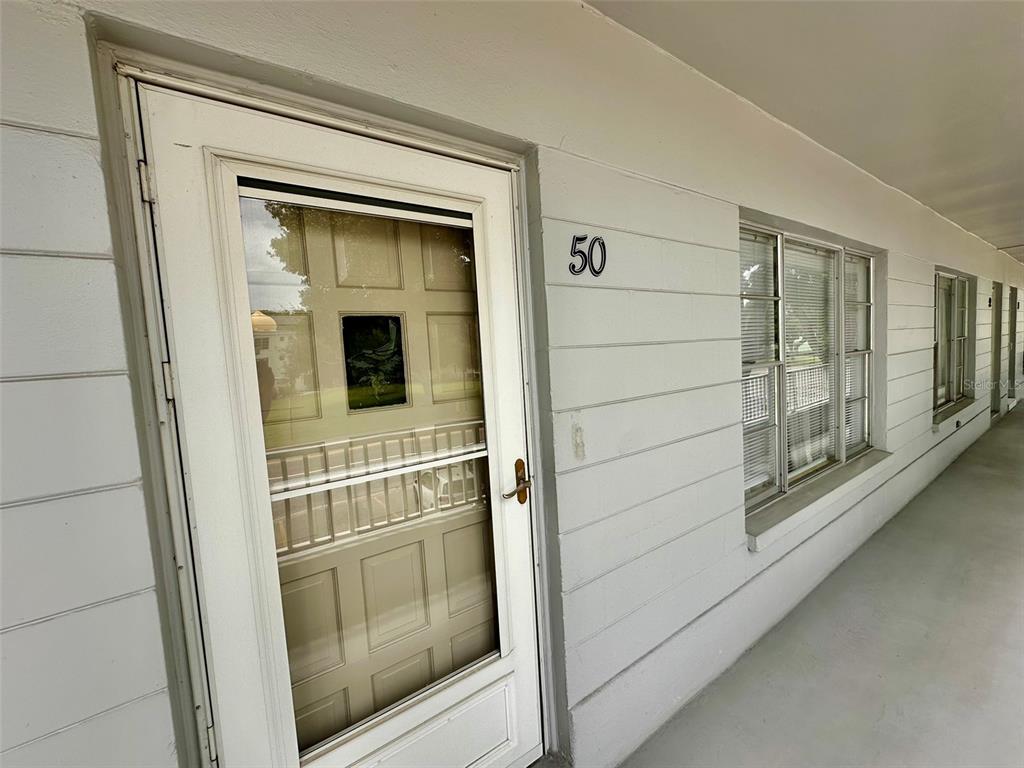 A white exterior door with a storm door and the number 50 on a walkway — 2100 WORLD PARKWAY BOULEVARD UNIT 50, CLEARWATER, FL