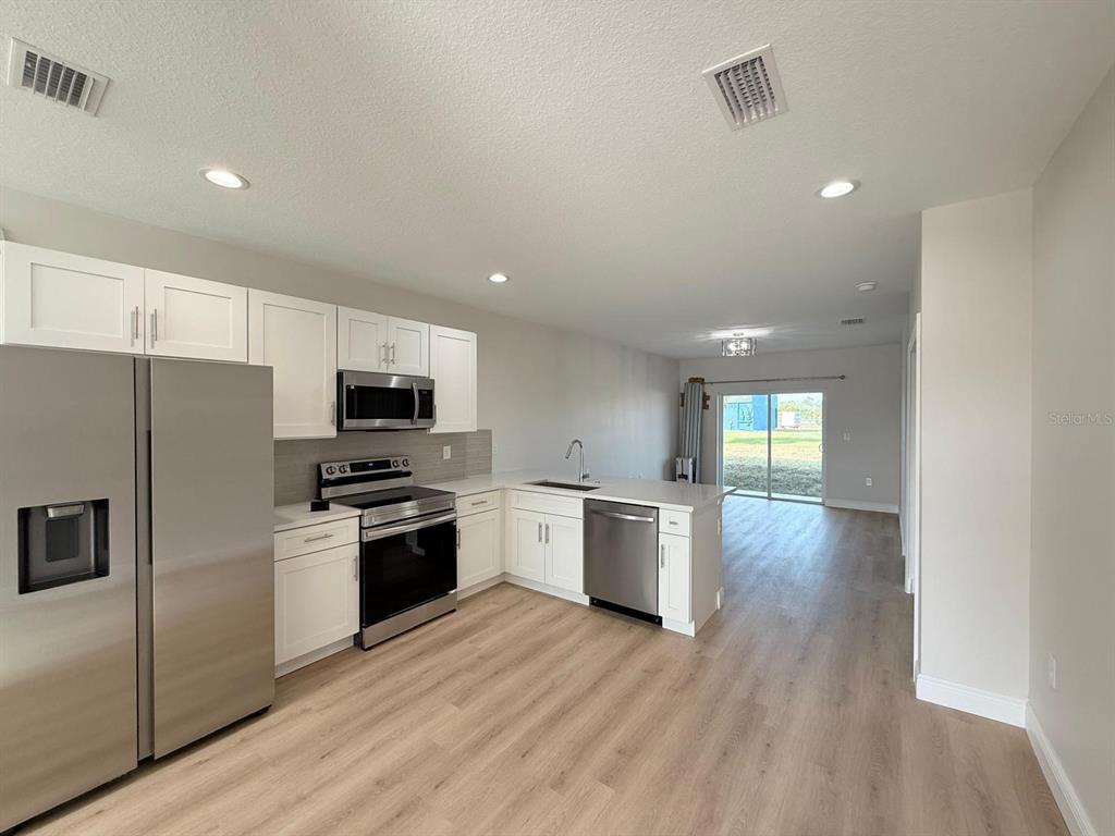 A modern kitchen features white cabinets, stainless steel appliances, and light wood-look flooring — 10336 PENDLETON AVENUE, ENGLEWOOD, FL
