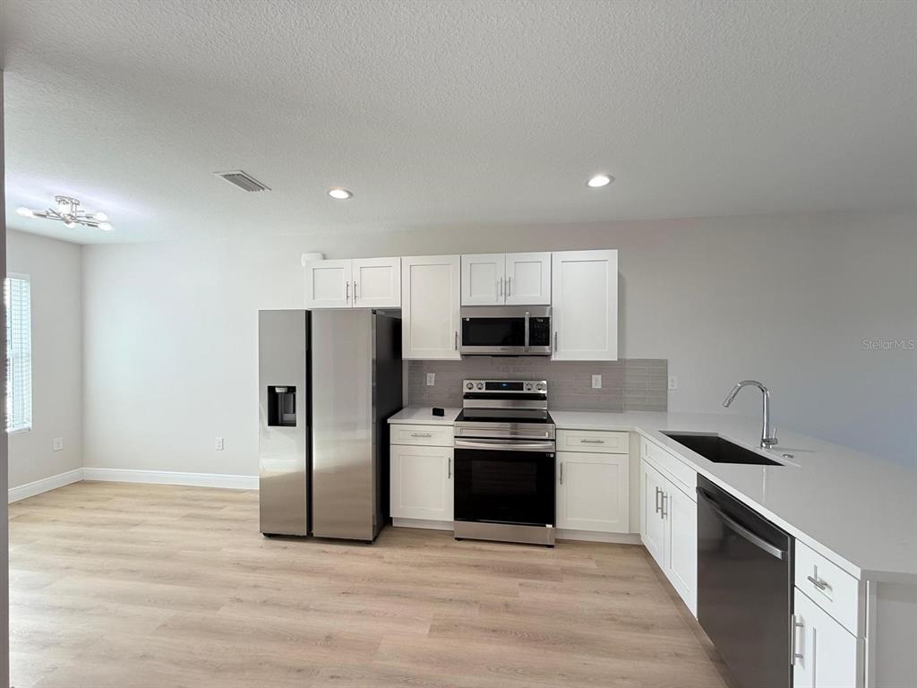 A kitchen features white cabinets, stainless steel appliances, a gray tile backsplash, and light wood flooring — 10336 PENDLETON AVENUE, ENGLEWOOD, FL