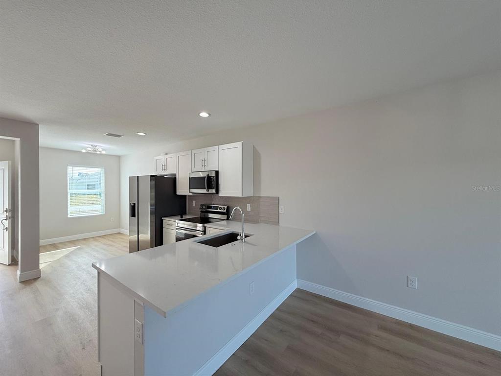 A kitchen features white cabinets, stainless steel appliances, and a quartz-topped island with a sink — 10336 PENDLETON AVENUE, ENGLEWOOD, FL