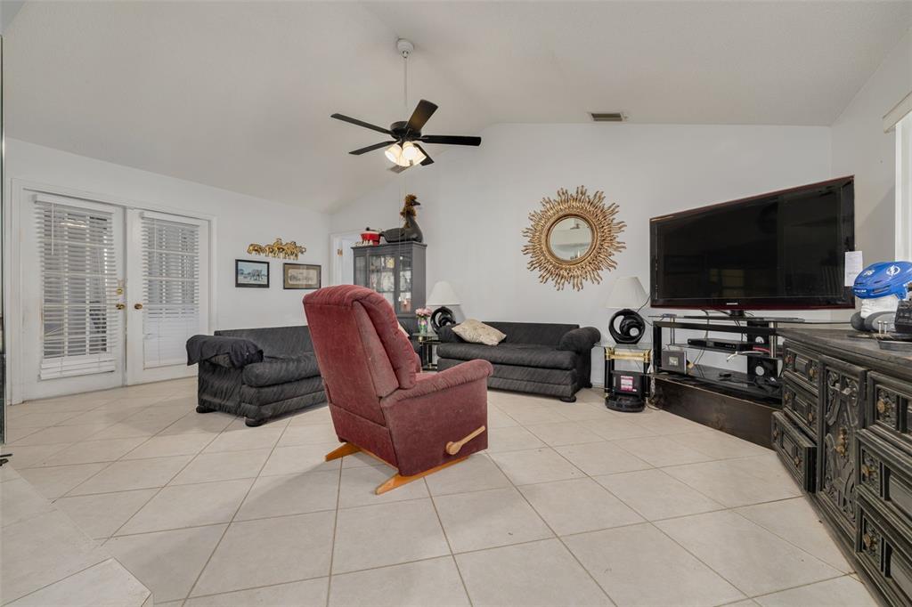 A living room features white walls, tile flooring, a ceiling fan, and black furniture — 1338 GREENLEA DRIVE, HOLIDAY, FL