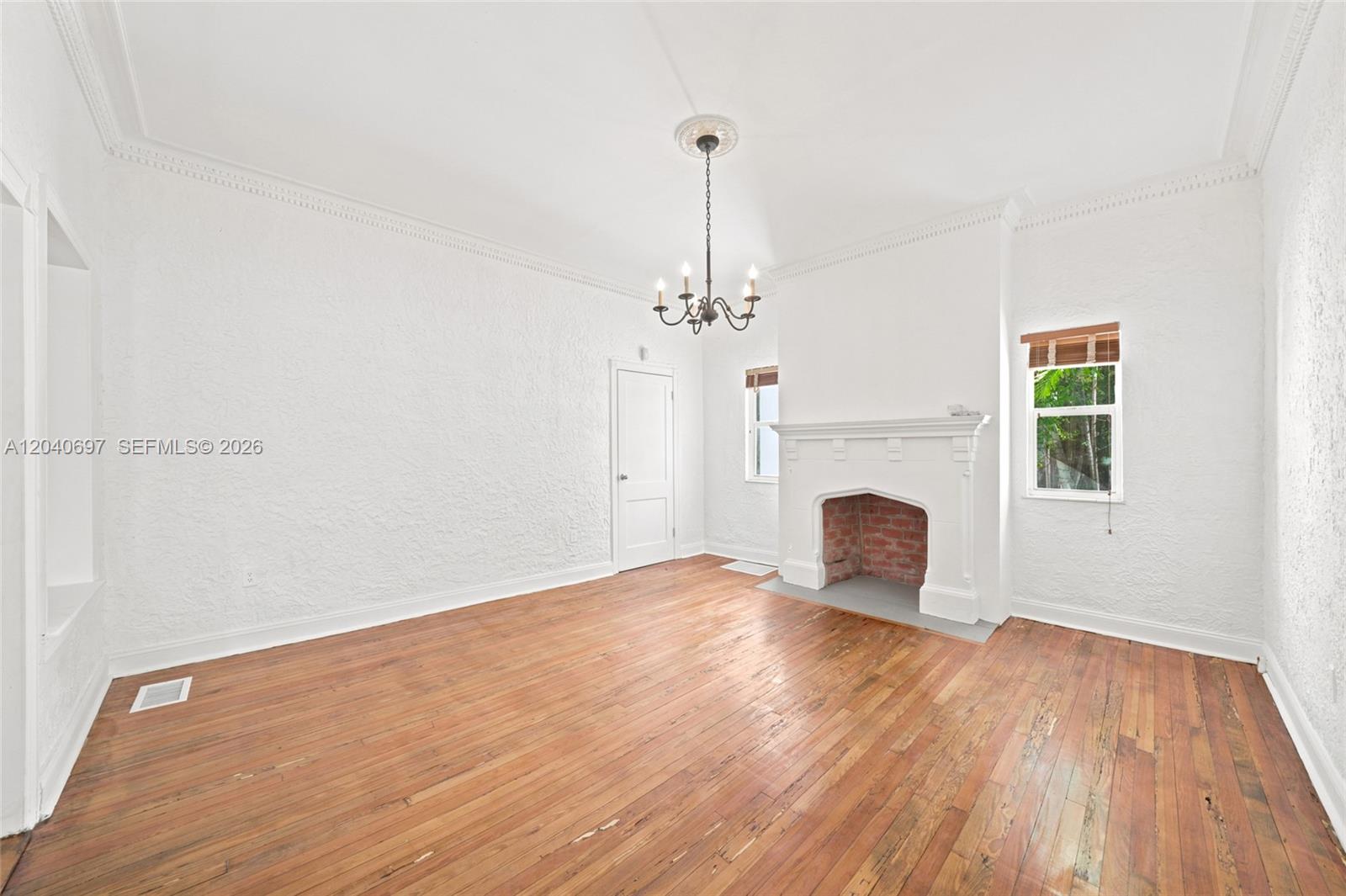 An empty room features white textured walls, a brick fireplace, and hardwood flooring — 160 NE 44th St # 1, Miami FL 33137, MIAMI, FL