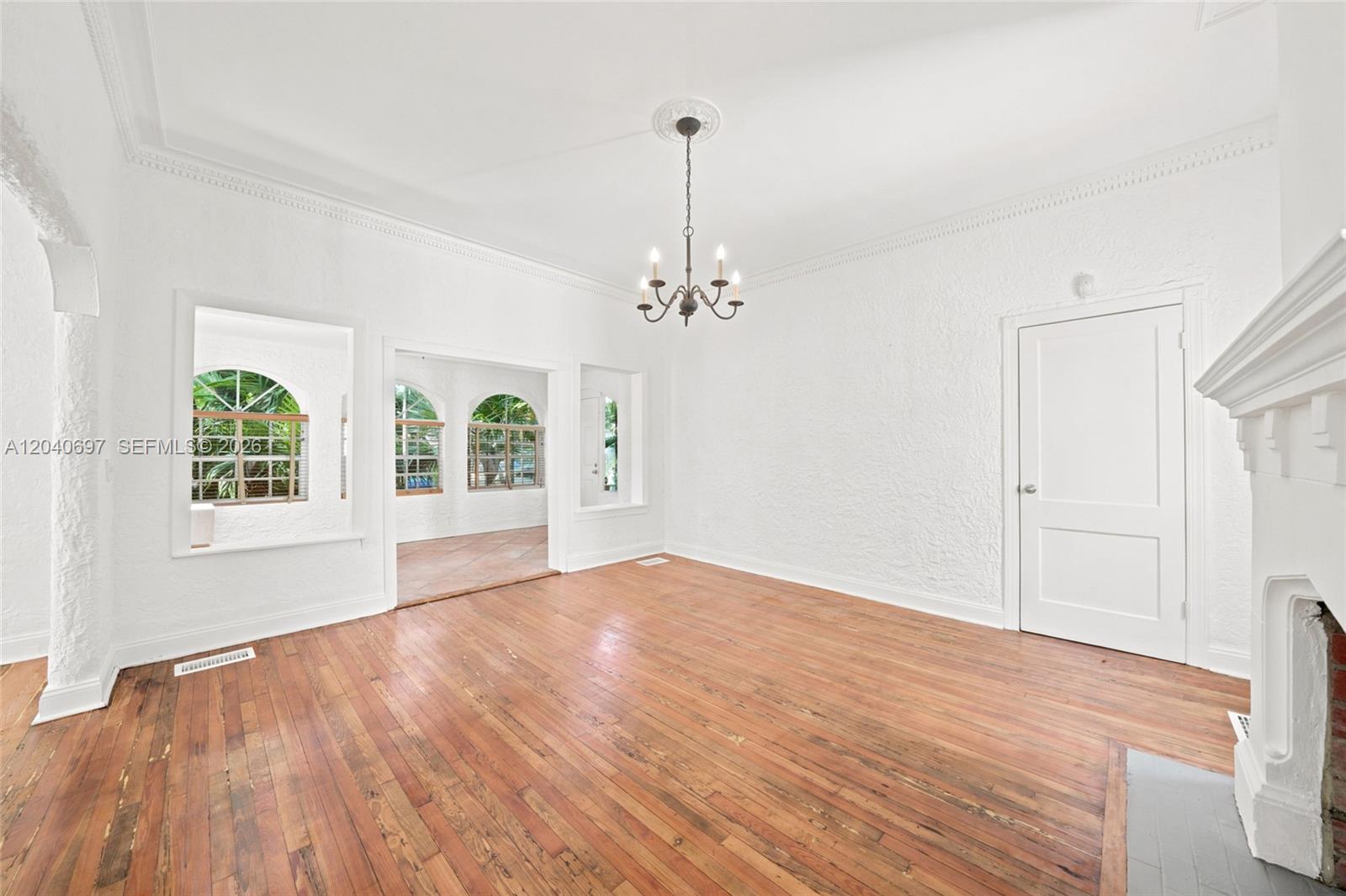 An empty living room features white textured walls, hardwood floors, and a chandelier — 160 NE 44th St # 1, Miami FL 33137, MIAMI, FL