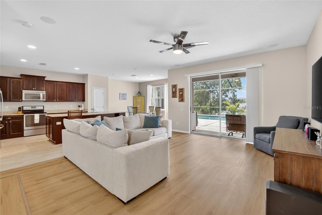 An open-concept living room and kitchen with wood-look flooring, a sectional sofa, and sliding glass doors — 6207 MAGNOLIA PARK BLVD, RIVERVIEW, FL