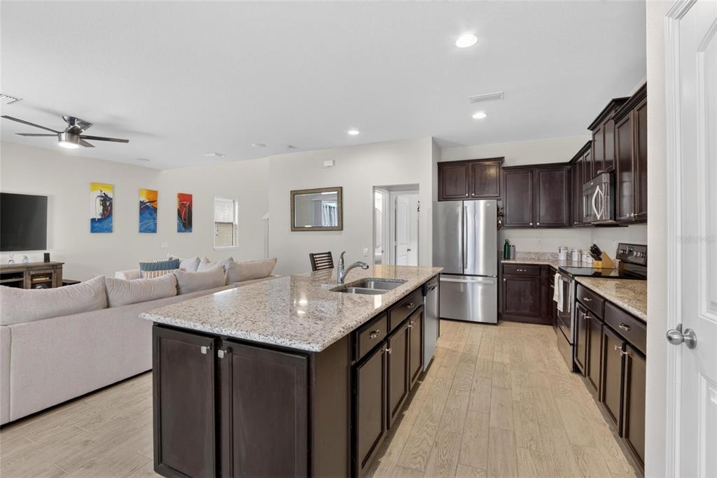 A kitchen with dark cabinets and granite countertops opens into a living room with seating — 6207 MAGNOLIA PARK BLVD, RIVERVIEW, FL