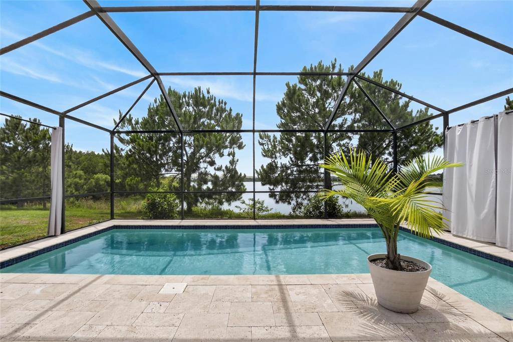 A screened-in swimming pool patio overlooks a lake surrounded by trees under a blue sky — 6207 MAGNOLIA PARK BLVD, RIVERVIEW, FL