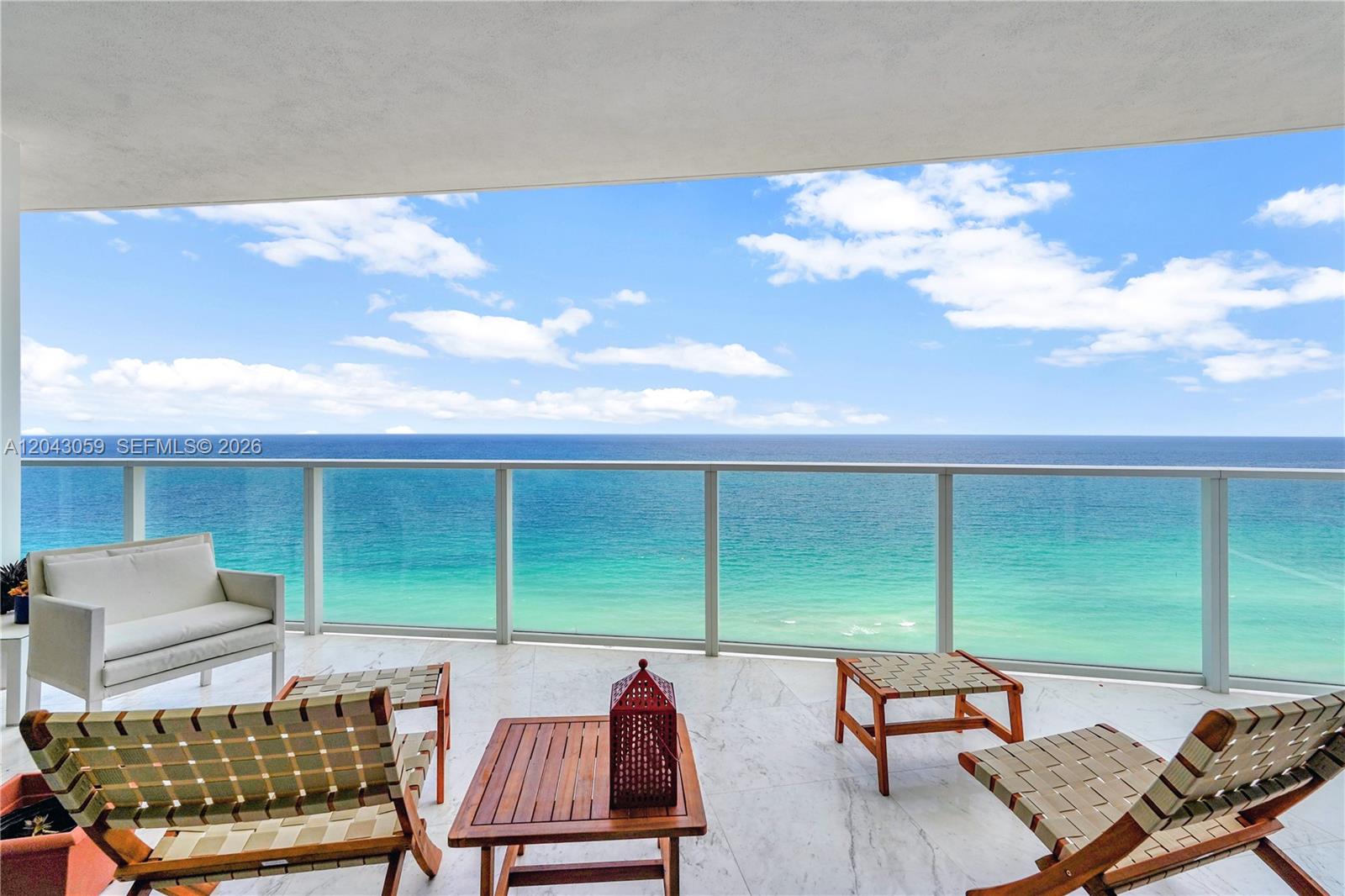 A balcony with marble flooring overlooks the ocean, featuring outdoor seating and a glass railing — 3951 S Ocean Dr # 1901, Hollywood FL 33019, HOLLYWOOD, FL