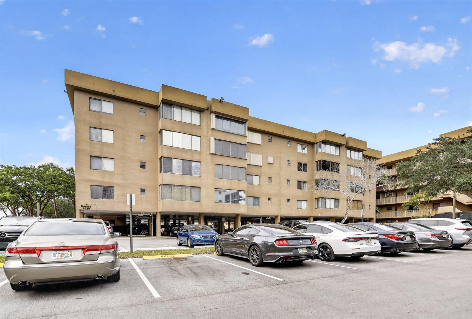 A multi-story tan apartment building stands behind a parking lot filled with several vehicles — 8030 Hampton Boulevard # 414, North Lauderdale FL 33068, NORTH LAUDERDALE, FL
