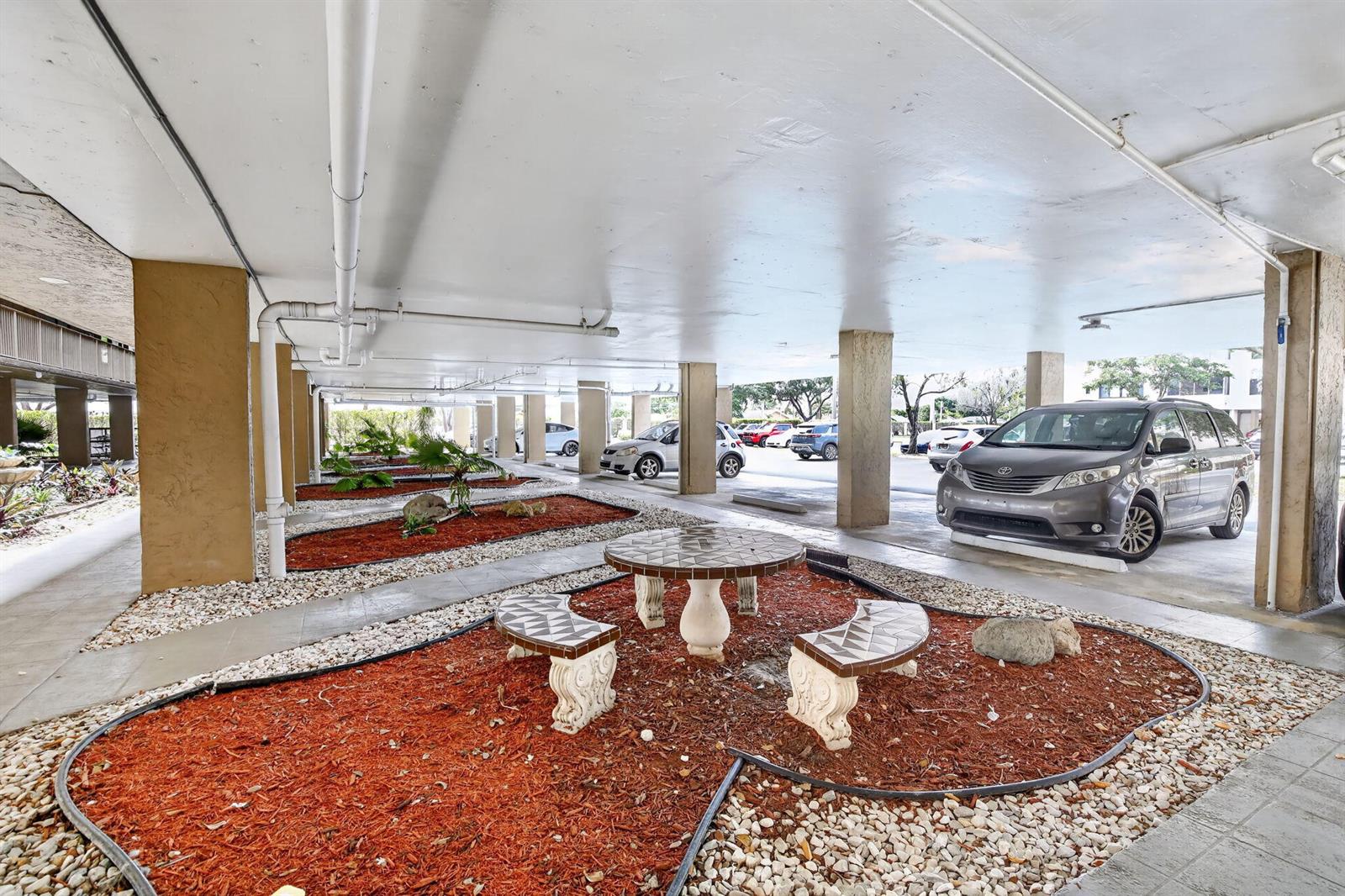 A covered parking area features a tiled table and benches set within a landscaped bed — 8030 Hampton Boulevard # 414, North Lauderdale FL 33068, NORTH LAUDERDALE, FL