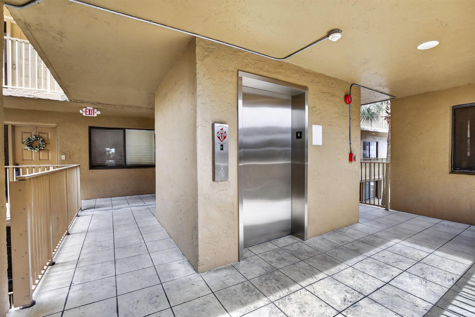 An outdoor apartment building hallway features a stainless steel elevator and tiled flooring — 8030 Hampton Boulevard # 414, North Lauderdale FL 33068, NORTH LAUDERDALE, FL