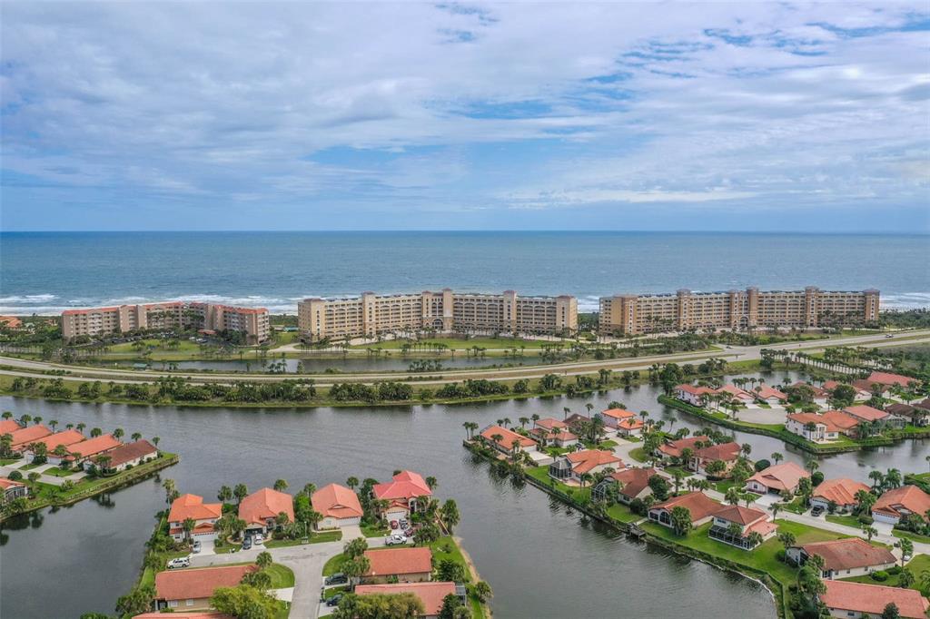 An aerial view shows a coastal residential community with houses, canals, and large beachfront hotels — 104 SURFVIEW DRIVE UNIT 1608, PALM COAST, FL