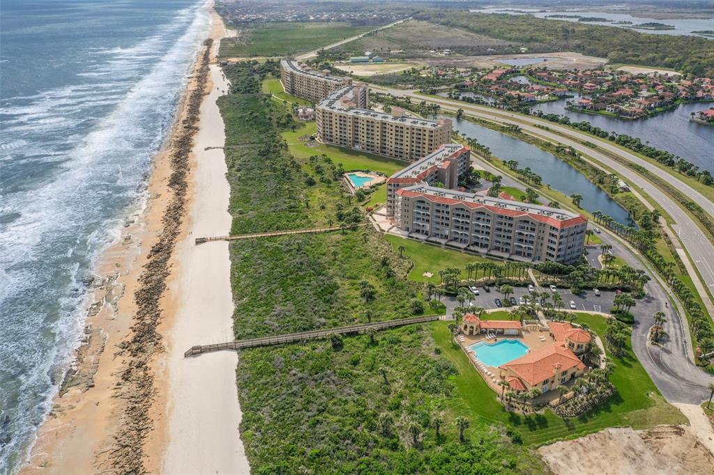 An aerial view of beachfront condominiums, a swimming pool, and a wooden boardwalk near dunes — 104 SURFVIEW DRIVE UNIT 1608, PALM COAST, FL