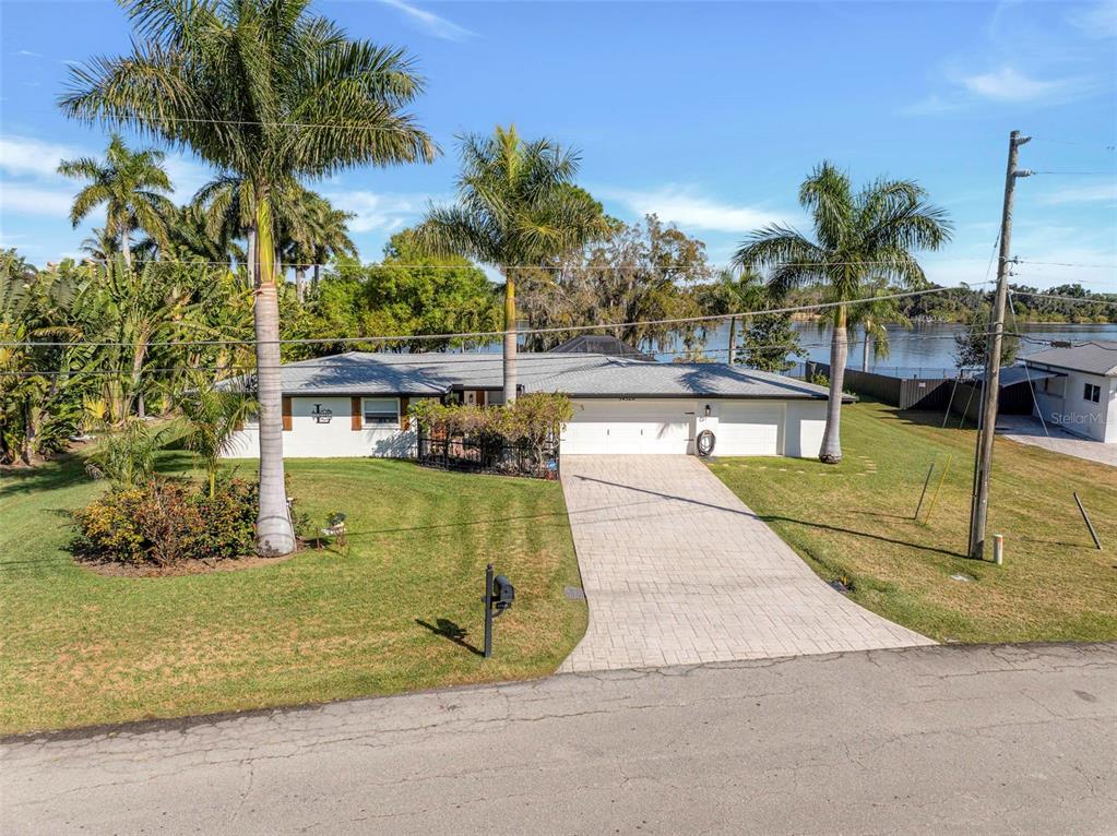 A single-story house with a paved driveway and palm trees sits along a waterfront — 14526 RIVERSIDE DRIVE, FORT MYERS, FL