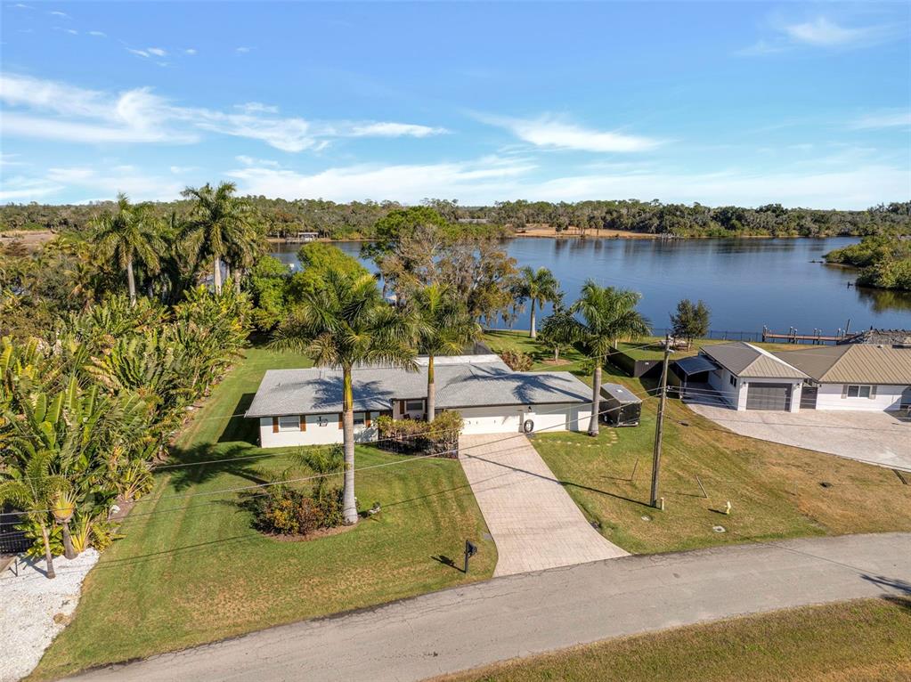 An aerial view of a single-story house with a paved driveway, palm trees, and lakefront — 14526 RIVERSIDE DRIVE, FORT MYERS, FL