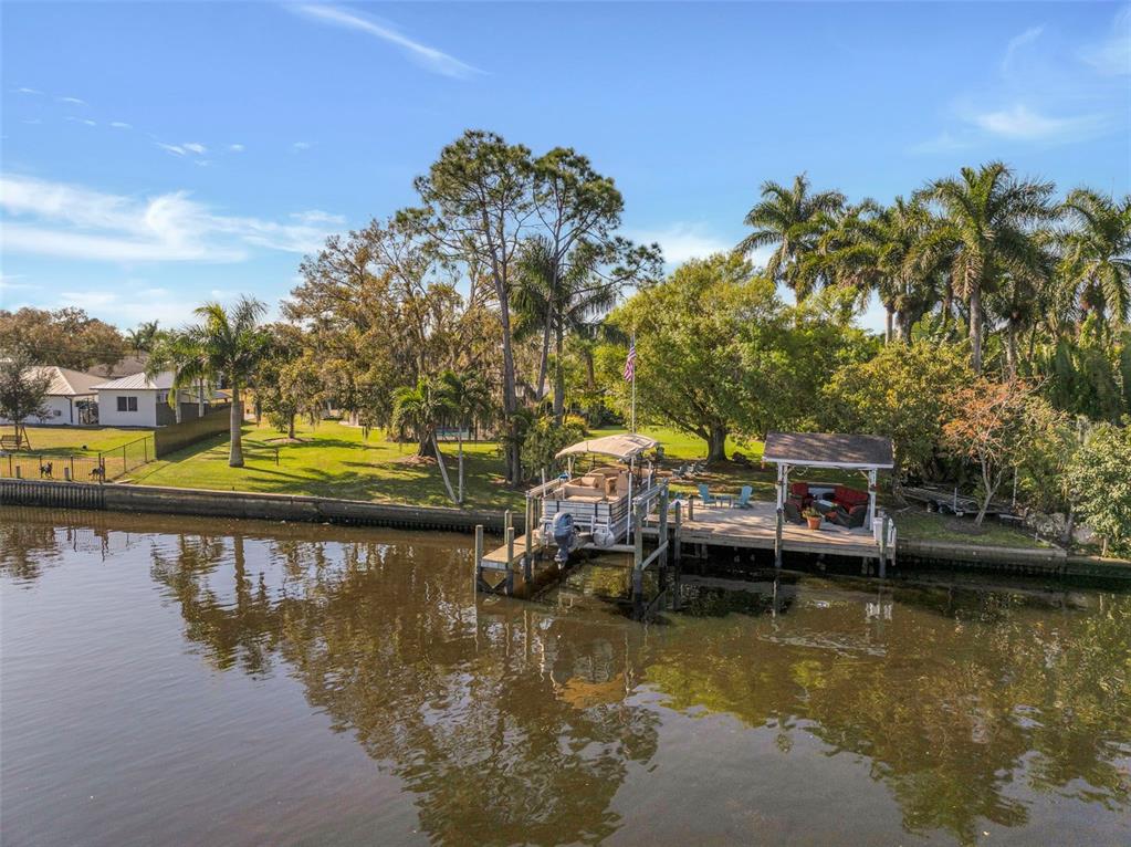 A pontoon boat is docked at a wooden pier along a canal near palm trees — 14526 RIVERSIDE DRIVE, FORT MYERS, FL