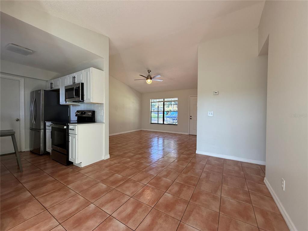 A kitchen with white cabinets and stainless steel appliances opens into a tiled living area — 7320 ANSTEAD CIRCLE, ORLANDO, FL