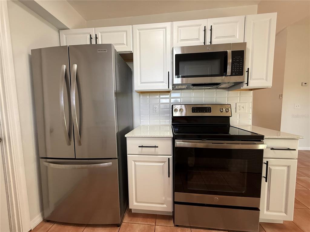 A kitchen features white cabinets, stainless steel appliances, and a tiled backsplash — 7320 ANSTEAD CIRCLE, ORLANDO, FL