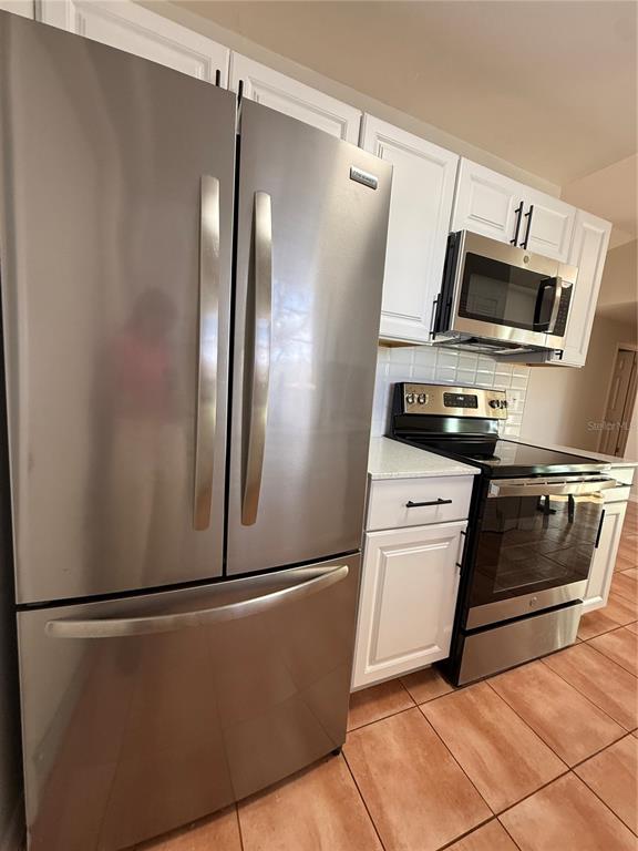A kitchen features stainless steel appliances, white cabinets, and light-colored countertops over tiled floors — 7320 ANSTEAD CIRCLE, ORLANDO, FL