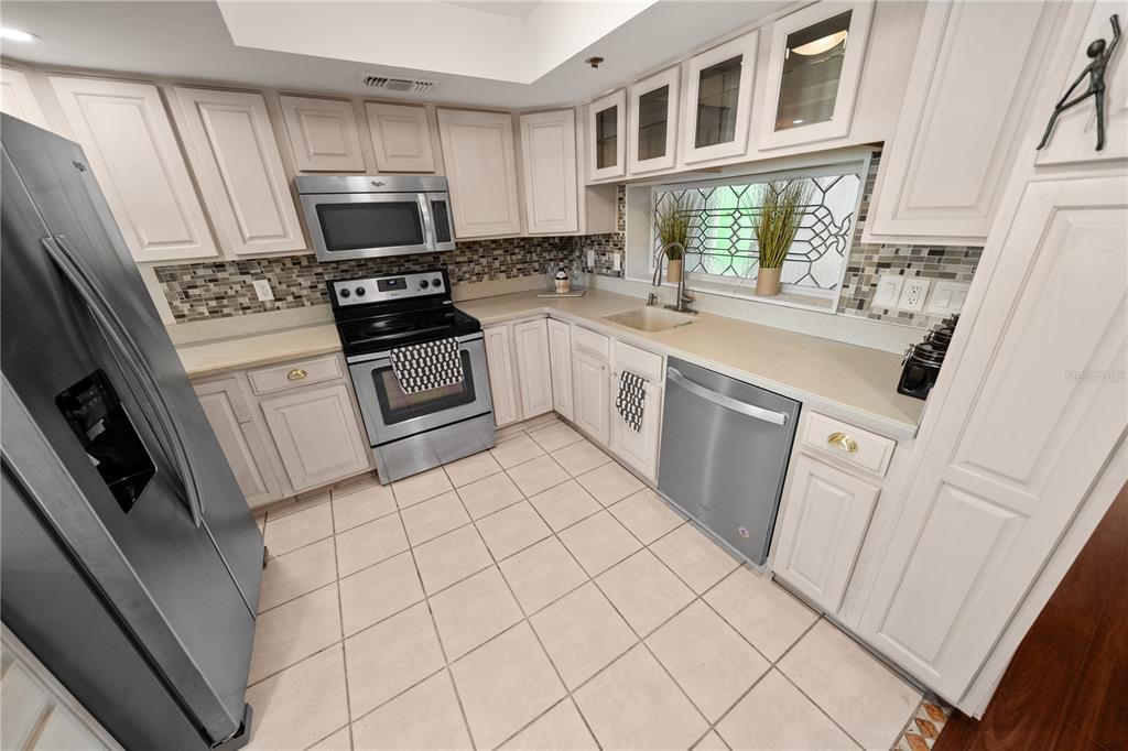 A kitchen features white cabinets, stainless steel appliances, a tiled backsplash, and light-colored floor tiles — 201 W LAUREL STREET UNIT 701, TAMPA, FL