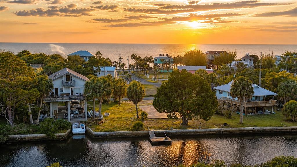 An aerial view shows two elevated houses near a canal with a sunset over the ocean — 10166 CABANA STREET, WEEKI WACHEE, FL