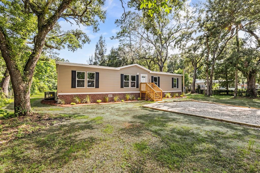 A single-story manufactured home with tan siding, brick skirting, and a gravel driveway — 25046 CELESTIAL STREET, CHRISTMAS, FL