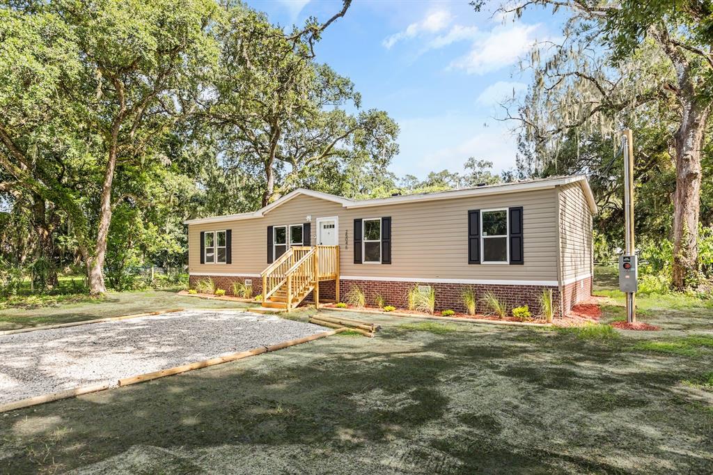 A single-story manufactured home with tan siding and a brick foundation sits on a lot — 25046 CELESTIAL STREET, CHRISTMAS, FL