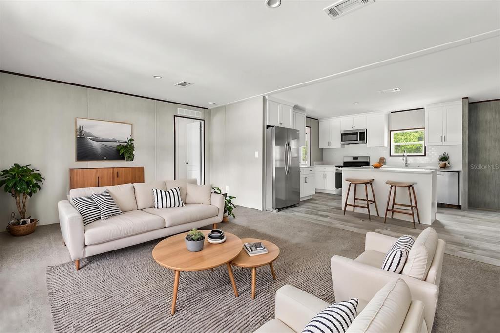 An open-concept living room and kitchen featuring white cabinetry, stainless steel appliances, and neutral furniture — 25046 CELESTIAL STREET, CHRISTMAS, FL