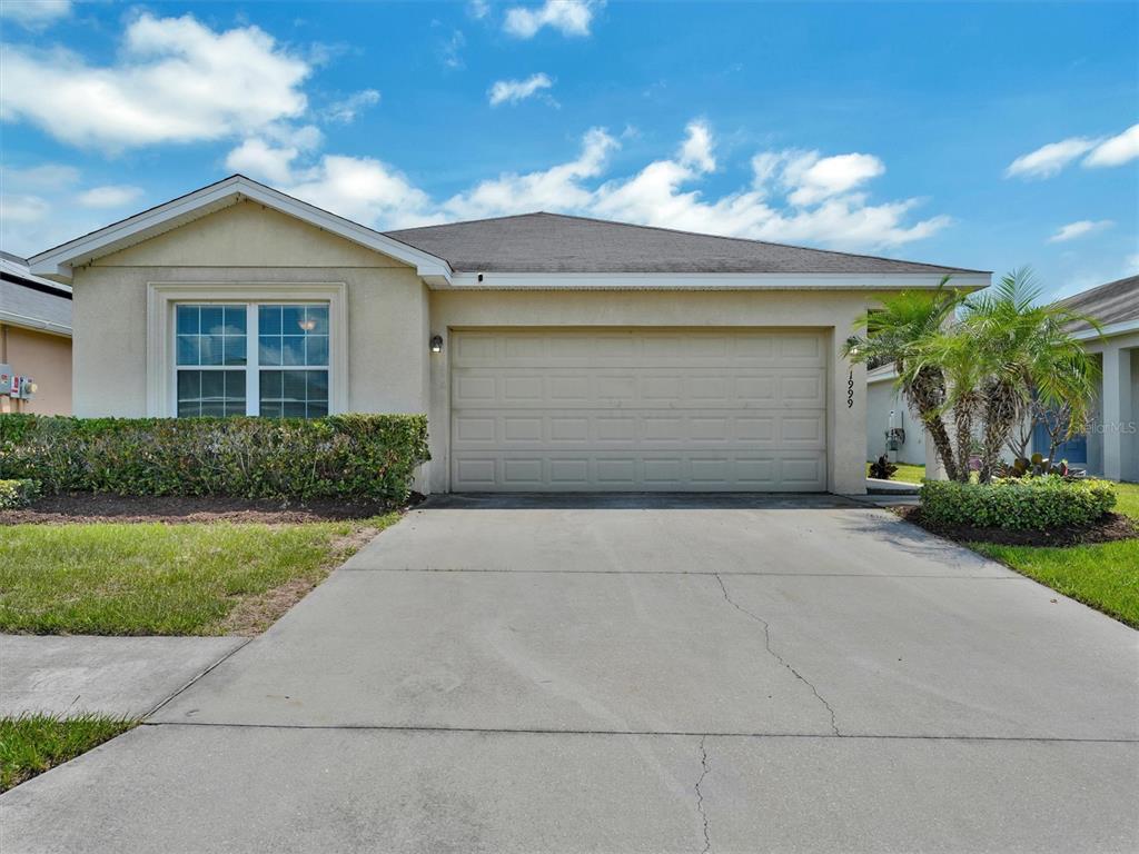 A single-story house features a beige stucco exterior, a two-car garage, and a concrete driveway — 1999 BRETTON RIDGE WAY, WINTER HAVEN, FL