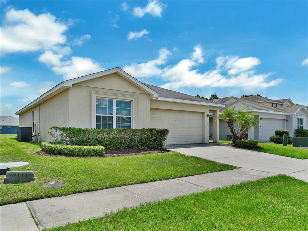 A single-story suburban house with a beige stucco exterior, a two-car garage, and a lawn — 1999 BRETTON RIDGE WAY, WINTER HAVEN, FL