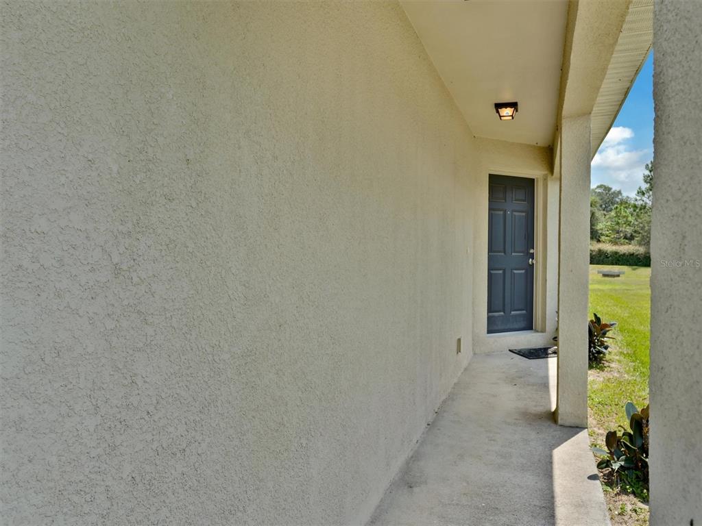 A covered concrete walkway leads to a dark gray door along a stucco exterior wall — 1999 BRETTON RIDGE WAY, WINTER HAVEN, FL