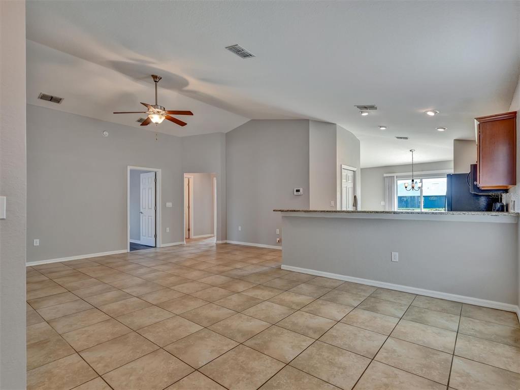An open-concept living area features light gray walls, tan tile flooring, and a kitchen breakfast bar — 1999 BRETTON RIDGE WAY, WINTER HAVEN, FL