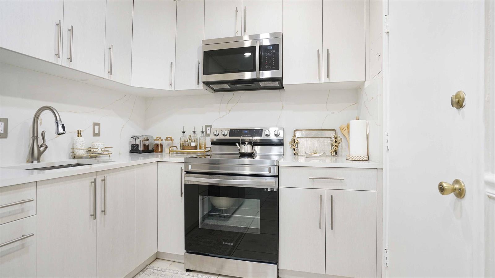 A modern kitchen features white cabinetry, stainless steel appliances, and a white marble-patterned backsplash — 400 S Cypress Road # 428, Pompano Beach FL 33060, POMPANO BEACH, FL
