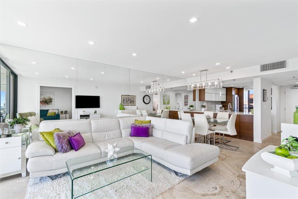A bright living room features a white sectional sofa, a glass coffee table, and mirrored walls — 2707 N Ocean Boulevard # D603, Boca Raton FL 33431, BOCA RATON, FL