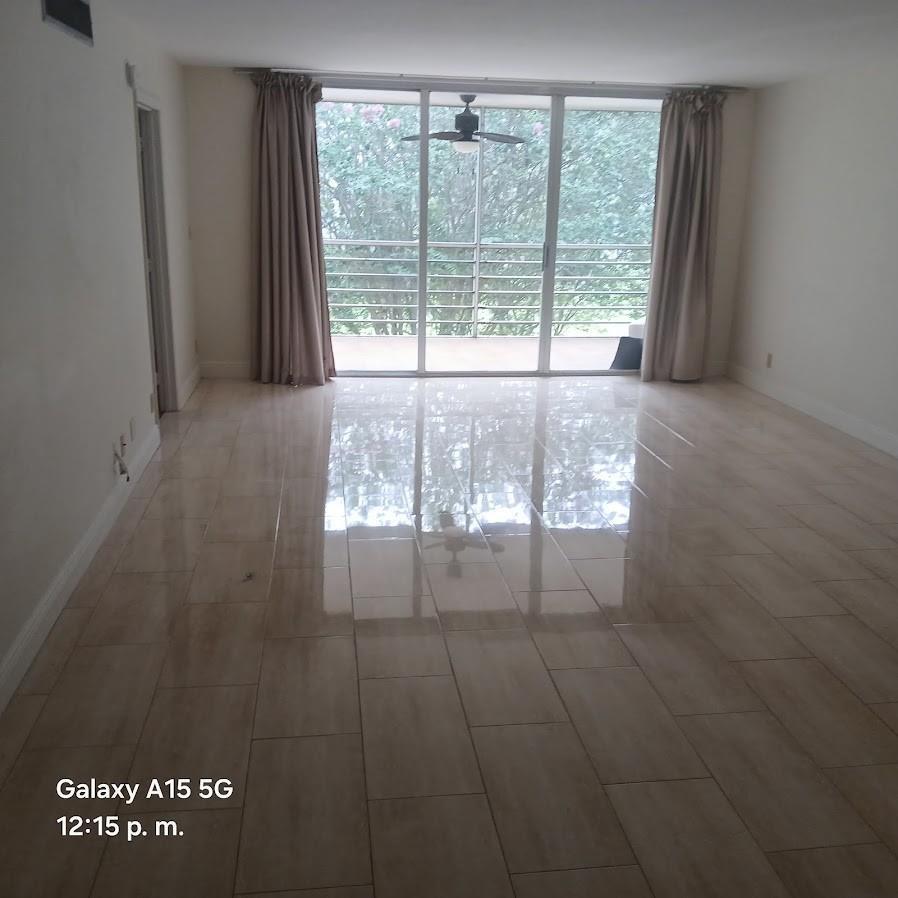 An empty room with light-colored tile flooring, beige curtains, and a sliding glass door balcony — 800 Cypress Grove Drive Unit 312, Pompano Beach FL 33069, POMPANO BEACH, FL