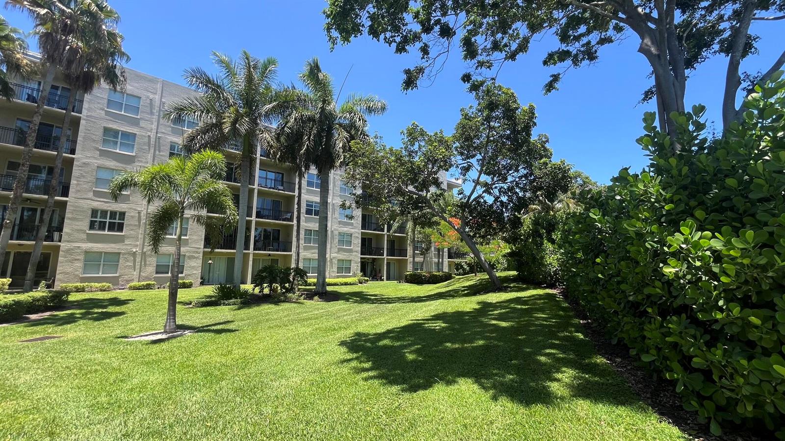 A multi-story apartment building stands behind a grassy lawn with palm trees and landscaping — 26 Royal Palm Way # 302, Boca Raton FL 33432, BOCA RATON, FL
