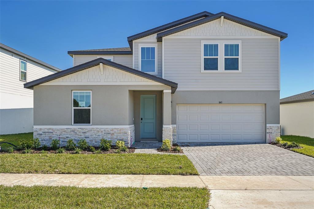 A two-story suburban house with a light-colored facade, stone veneer base, and a paved driveway — 843 SUNSHOWER DRIVES, LADY LAKE, FL