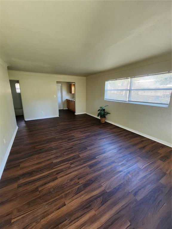 An empty living room features dark wood-look flooring, light-colored walls, and a large window — 2219 HIGHLAND STREET UNIT 1, ST PETERSBURG, FL