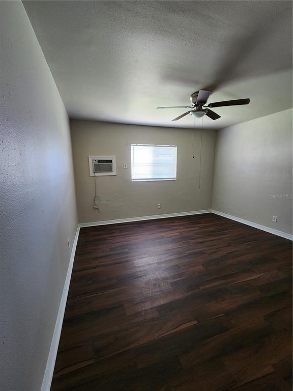 An empty room with dark wood-look flooring, a ceiling fan, and a wall-mounted air conditioner — 2219 HIGHLAND STREET UNIT 1, ST PETERSBURG, FL